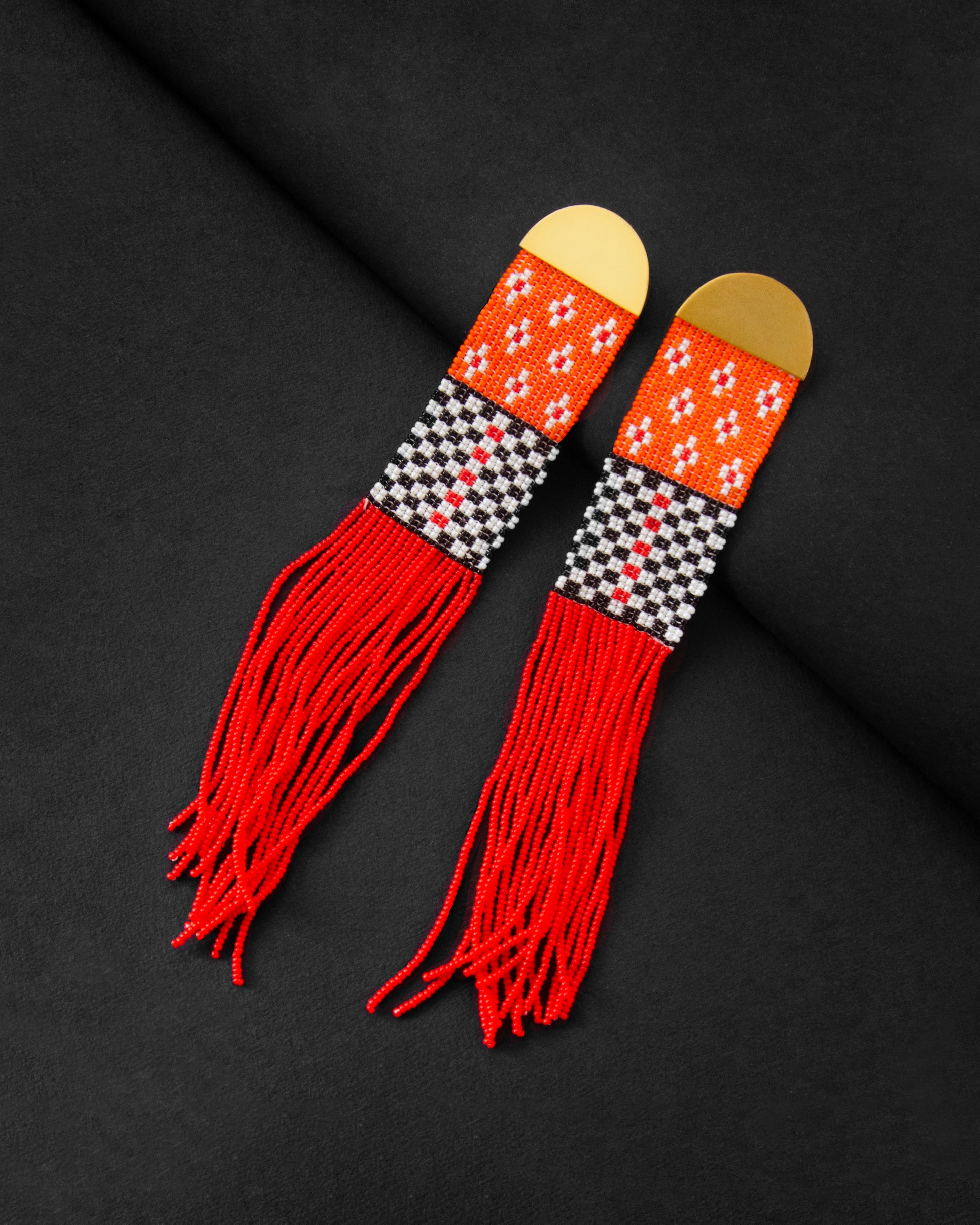 Pair of earrings with red fringes and geometric patterns on a black background