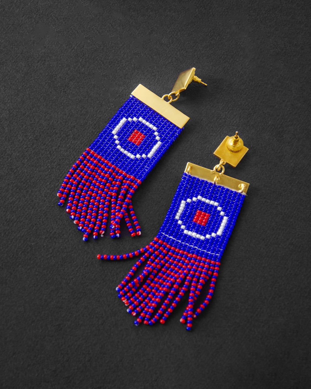 Pair of beaded earrings with blue, red, and gold design on a dark background